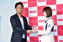 株式会社レコチョクの執行役員・柴崎栄太郎氏（左）よりトロフィーを受け取る佐々木美玲（右）。