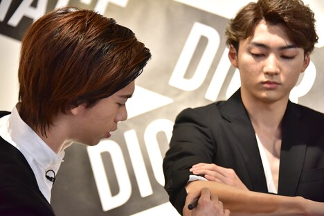 ユーキ（右）の腕にリキッドファンデーションを塗るリョウガ（左）。