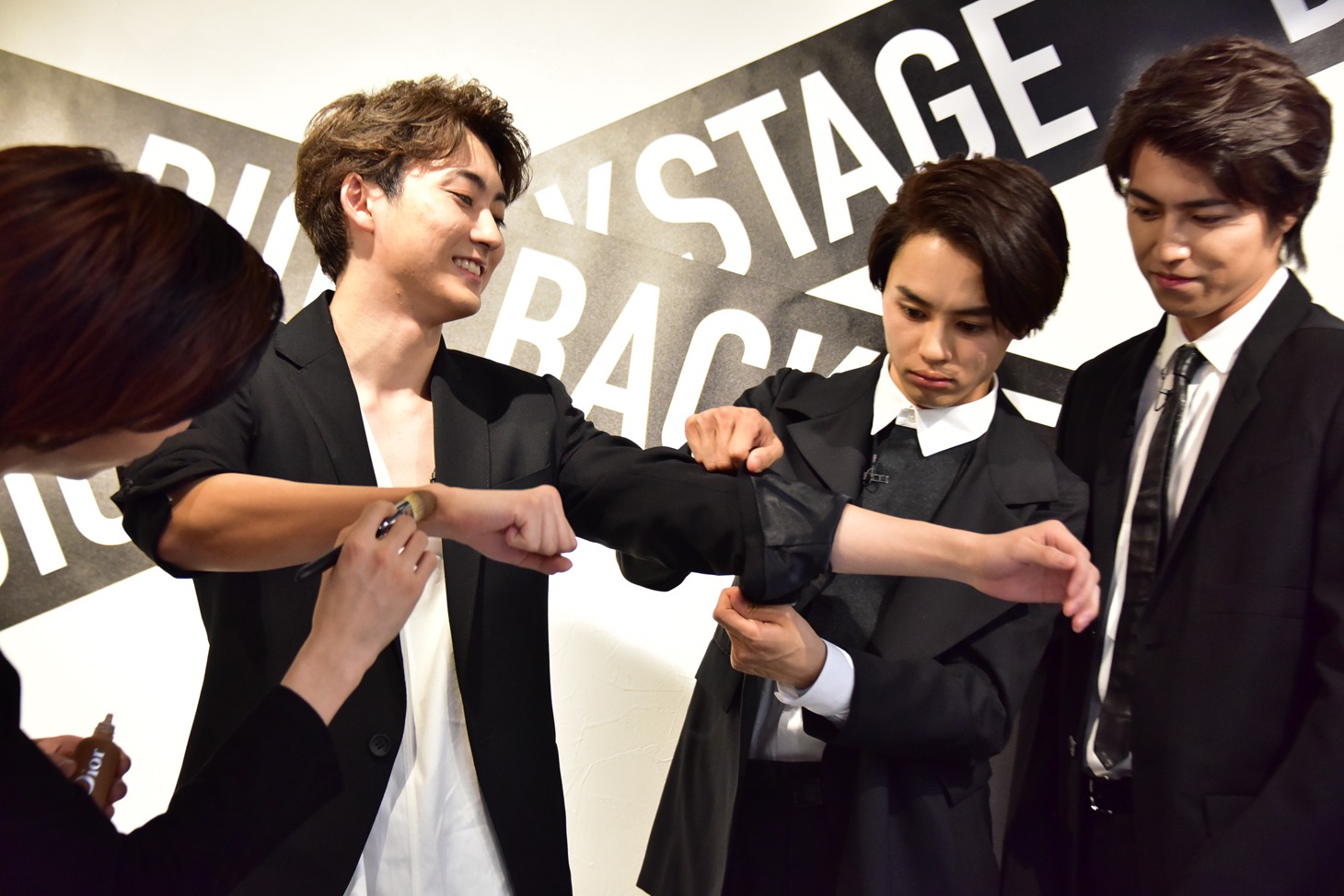 リョウガに右腕をメイクしてもらい、タクヤに左腕を腕まくりしてもらうユーキ（左から2番目）と、3人を見守るタカシ（右）。
