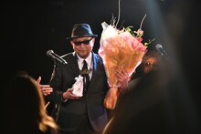 花束と饅頭を手にステージを降りるBro.TOM。