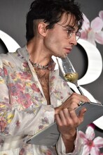 シャンパングラスのペンでメモを取るエズラ・ミラー。