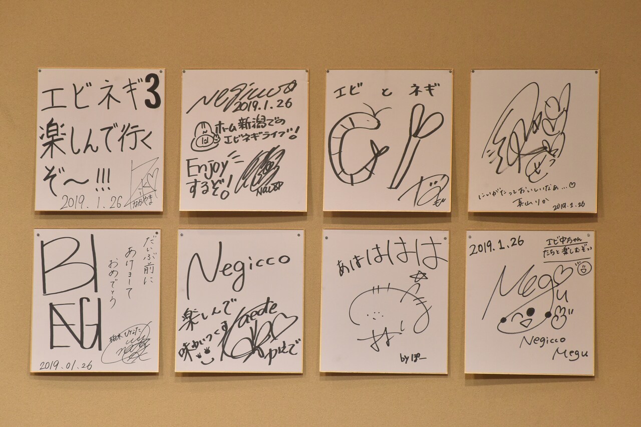 こたつの後ろに飾られたエビネギメンバーのサイン色紙。 - Negicco