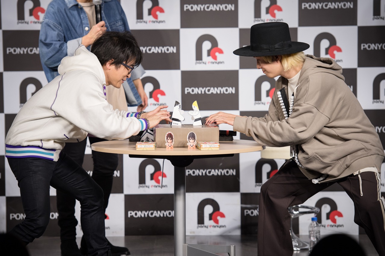 紙相撲で勝負する阿部敦と山田義孝（Vo）。（撮影：星野耕作）