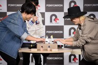 紙相撲で勝負する吉田結威（G, Vo）と山田義孝（Vo）。（撮影：星野耕作）