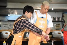 関口メンディー（左）が振るフライパンにケチャップを入れる佐野玲於（右）。