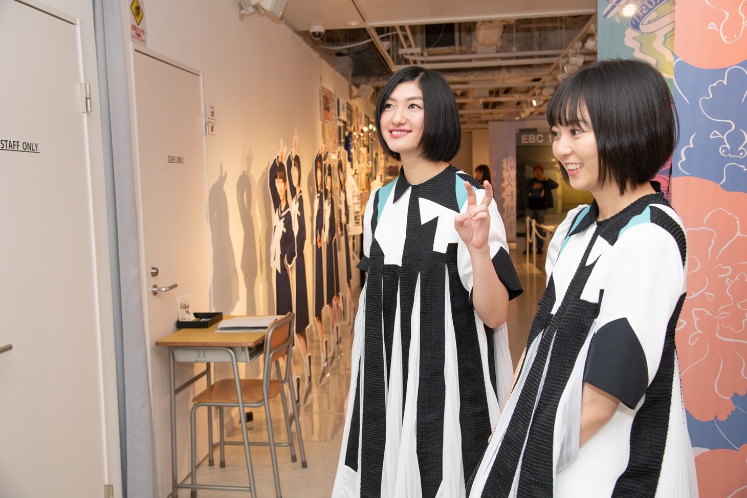 パネルにサインを書き入れるメンバーを見つめる小林歌穂（左）と安本彩花（右）。