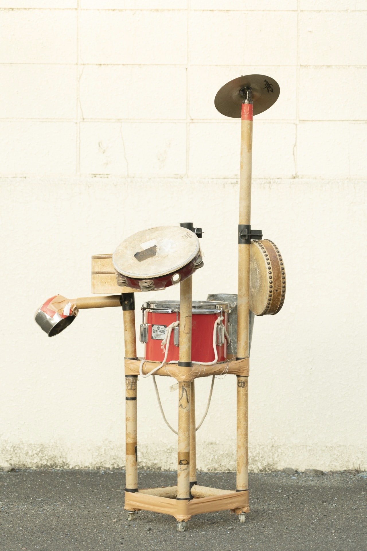 自作の日用品パーカッション。正面から見ると組み立て式のポール部分に目、鼻、口が描かれている。