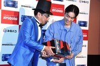 JOYSOUNDの社長（左）から「JOYSOUND MAX GO」をプレゼントされた菅田将暉。