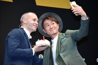 アンドレス・イニエスタ（左）とセルフィーを撮るナオト・インティライミ（右）。イニエスタが手にしているのはJリーグデビュー1周年をお祝いするケーキ。