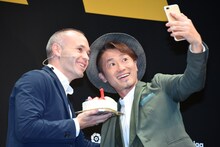 アンドレス・イニエスタ（左）とセルフィーを撮るナオト・インティライミ（右）。イニエスタが手にしているのはJリーグデビュー1周年をお祝いするケーキ。