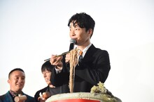 金色の箸で蕎麦を持ち上げる星野源。