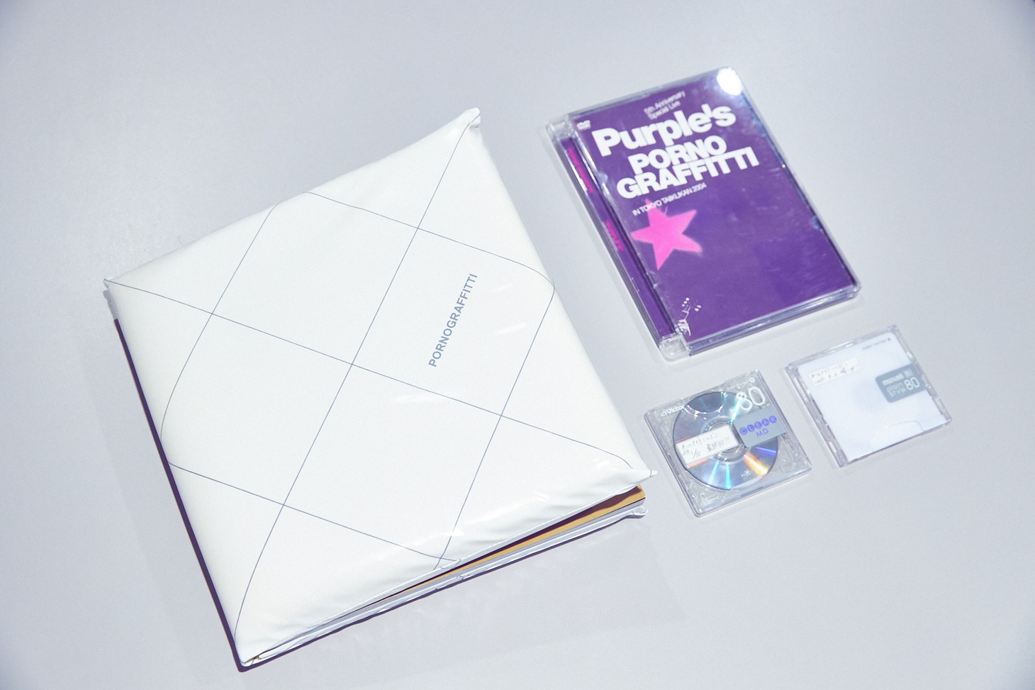 左から時計周りに写真集「LIVE PHOTO BOOK 東京ロマンスポルノ'09 ～愛と青春の日々～」、ライブDVD「5th Anniversary Special Live "PURPLE'S" IN TOKYO TAIIKUKAN 2004」、「ポルノグラフィティ岡野昭仁のオールナイトニッポン」が録音されたMD。