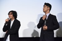 行定勲監督（左）が小林直己（右）の“首の太さ”について語る背後で襟元を整える小林直己。