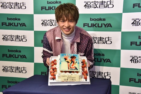 「STEP BY STEP」表紙がデザインされたバースデーケーキと佐藤大樹。