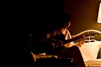 ベッドに腰掛けて歌う宮崎朝子。（撮影：河上良）