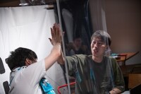 パーテーション越しにハイタッチするグランジ遠山（左）とはんにゃ金田（右）。