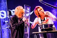 熱湯消毒したスイカを口に運ぼうとする喜矢武豊（右 / Gita-）と、それをシールド越しに見守る鬼龍院翔（左 / Vo-karu）。（撮影：菅沼剛弘）