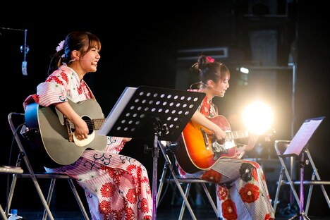 アコースティックギターで弾き語りする鈴木萌花と愛来。（写真提供：スターダストプロモーション）