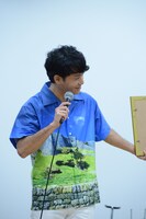 うるま市にある世界遺産・勝連城跡の写真がプリントされたかりゆしウェアをアピールする新里英之（Vo, G）。