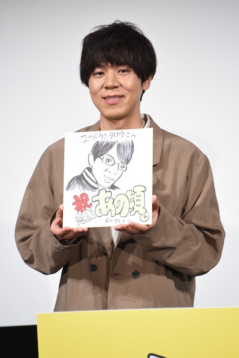 劔樹人による似顔絵を手にするコカドケンタロウ。