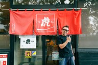 のれんの前でポーズを決めるKENさん。