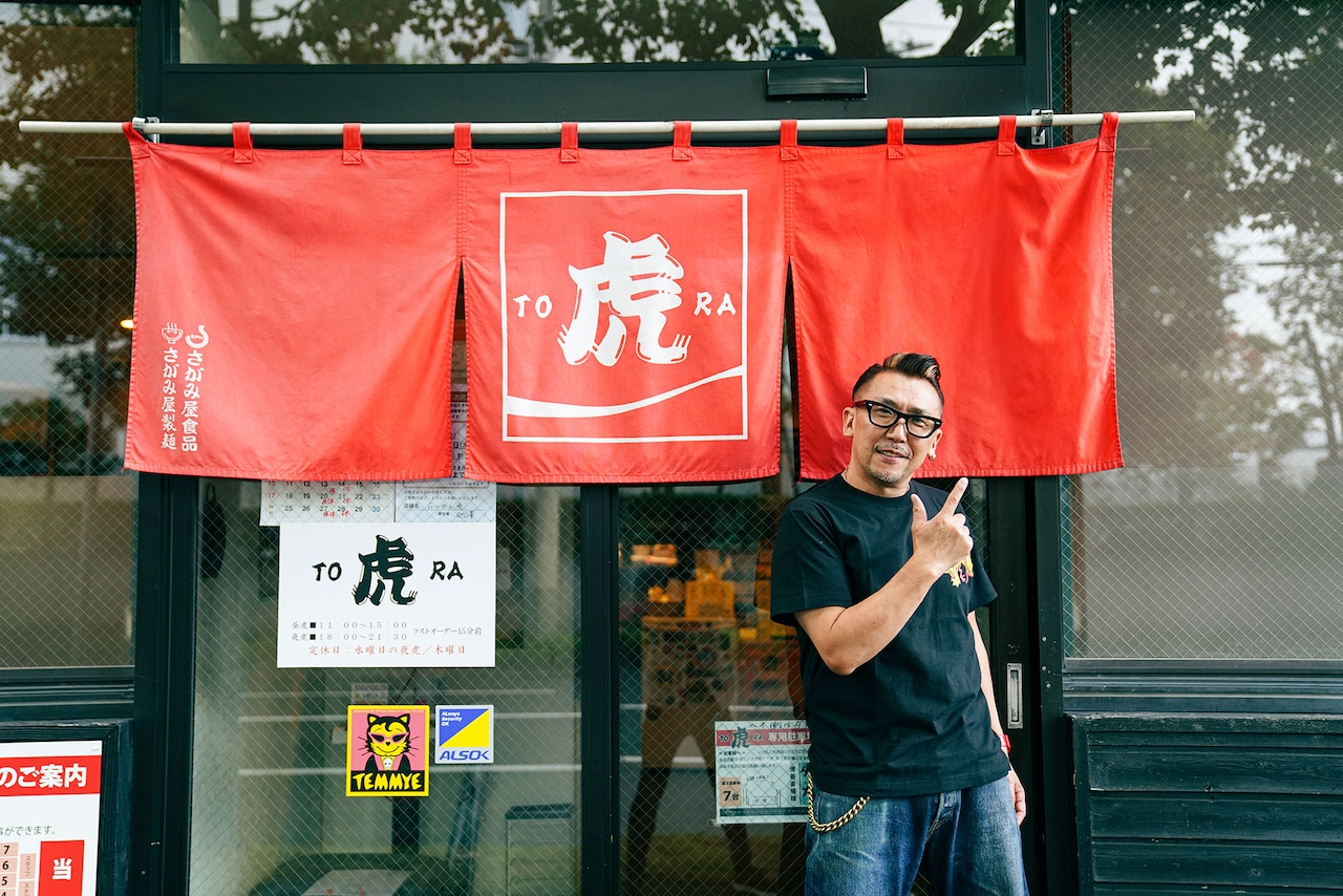 のれんの前でポーズを決めるKENさん。