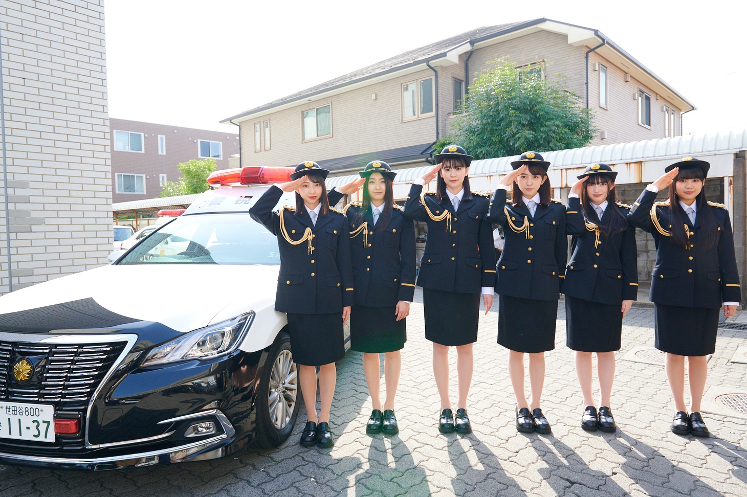 パトカーの横で敬礼する超ときめき♡宣伝部。