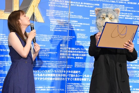 「劇場版ラジエーションハウス」の主題歌「More Than Words」に込めた思いをホワイトボードに書くMAN WITH A MISSIONのKamikaze Boy（右）とそれを覗き込む本田翼（左）。