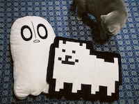 のっちさんが購入した「UNDERTALE」グッズ。左からナプスタブルーク、うざいイヌのぬいぐるみクッション。
