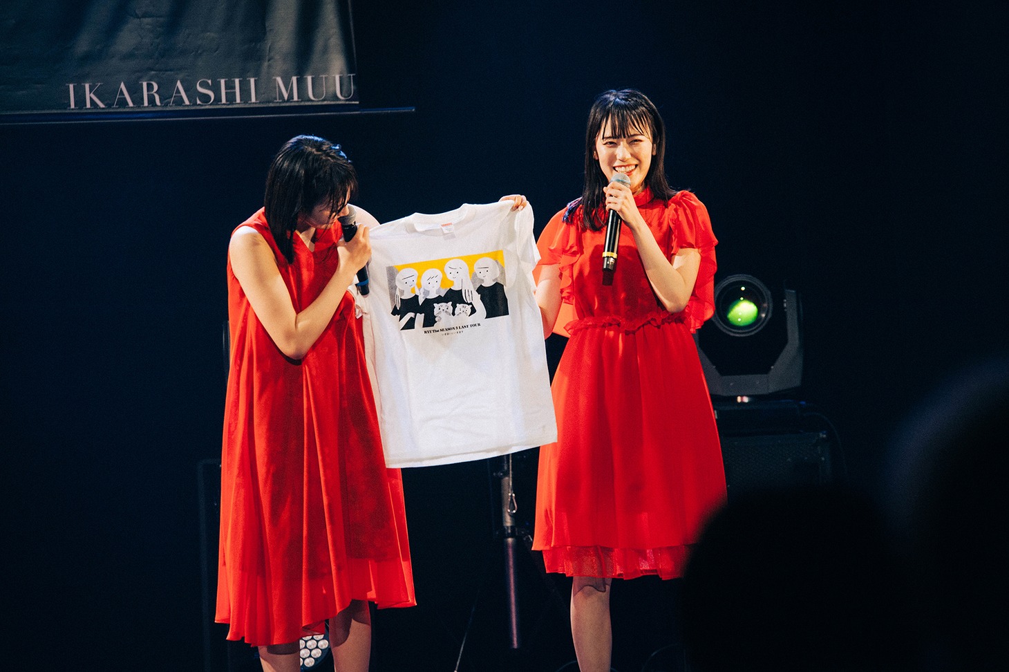 イラストレーターのkilldiscoがデザインしたグッズTシャツを紹介する横山実郁と佐藤乃々子。メンバー4人と佐藤の愛猫が描かれている。（撮影：垂水佳菜）