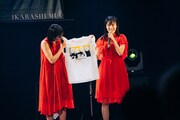 イラストレーターのkilldiscoがデザインしたグッズTシャツを紹介する横山実郁と佐藤乃々子。メンバー4人と佐藤の愛猫が描かれている。(撮影:垂水佳菜)