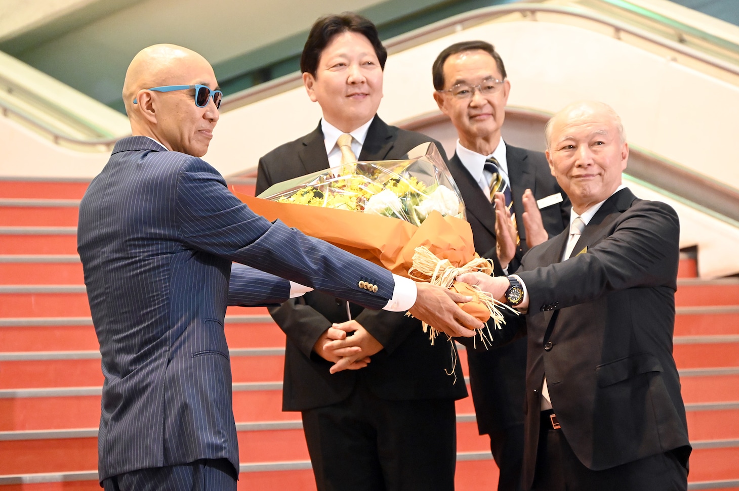中野サンプラザの金野晃代表取締役会長（右）に花束を贈呈するサンプラザ中野くん（左）。