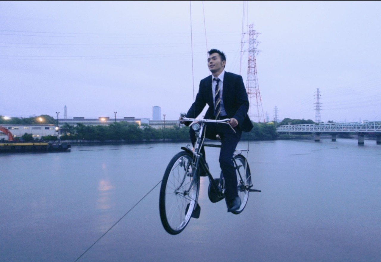 自転車に乗って空を飛ぶ玉置周啓（Vo, G）。
