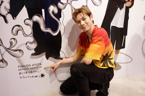 しゃがんで自分のサインを指差す福田歩汰。