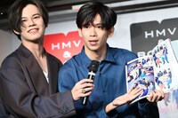 自身の引き伸ばされた顔を報道陣に紹介するリョウガ（右）。