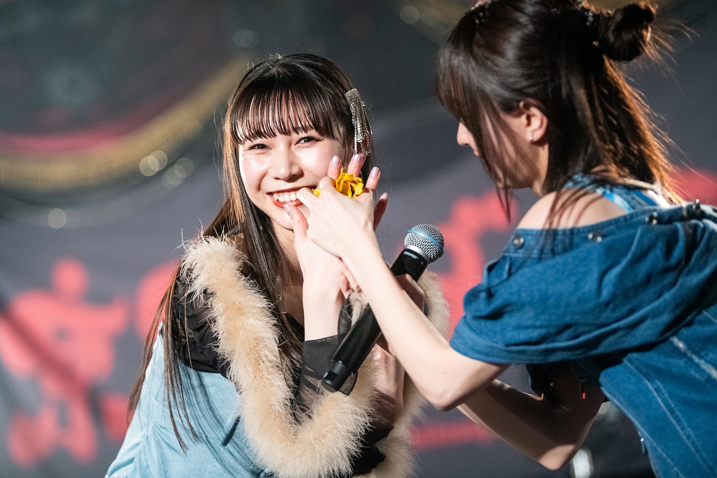 佐藤まりあ（右）にヒマワリを装着してもらう庄司芽生（左）。（撮影：音楽ナタリー編集部）