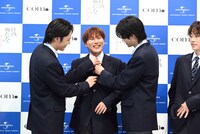 記者からネクタイが曲がっていることを指摘され、メンバーに直されるあむぎり（中央）。