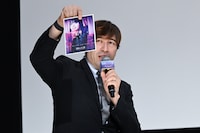 入場者プレゼント第2弾を持つ司会のサッシャ。