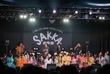 ステージ上で電話をかけ次回の出演交渉をするヤマモトショウ(後列右端)と電話を受ける宮野弦士(後列左端)。