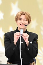 「推し生存」御守を手にするタカシ。