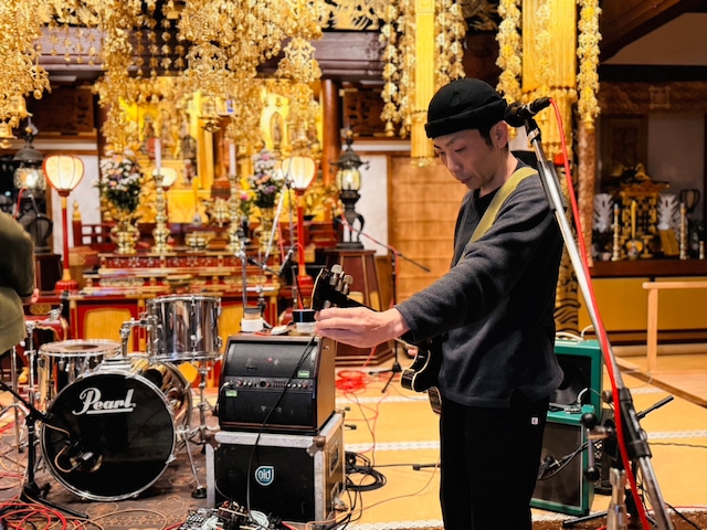 大慶寺でギターを弾く古里おさむ（風呂敷）。