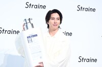 ボトルの巨大モックの裏面をカメラマンに見せておどける山下智久。