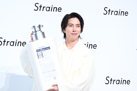 ボトルの巨大モックの裏面をカメラマンに見せておどける山下智久。