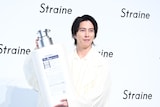 ボトルの巨大モックの裏面をカメラマンに見せておどける山下智久。