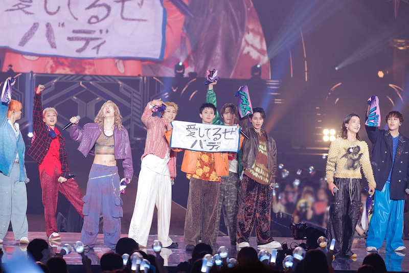 「愛してるぜバディ」と書いたタオルを掲げるBUDDiiS。