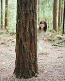 松田里奈（櫻坂46）1st写真集「まつりの時間」より、木陰から顔を出す松田里奈。（撮影：北浦敦子）