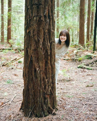松田里奈（櫻坂46）1st写真集「まつりの時間」より、木陰から顔を出す松田里奈。（撮影：北浦敦子）