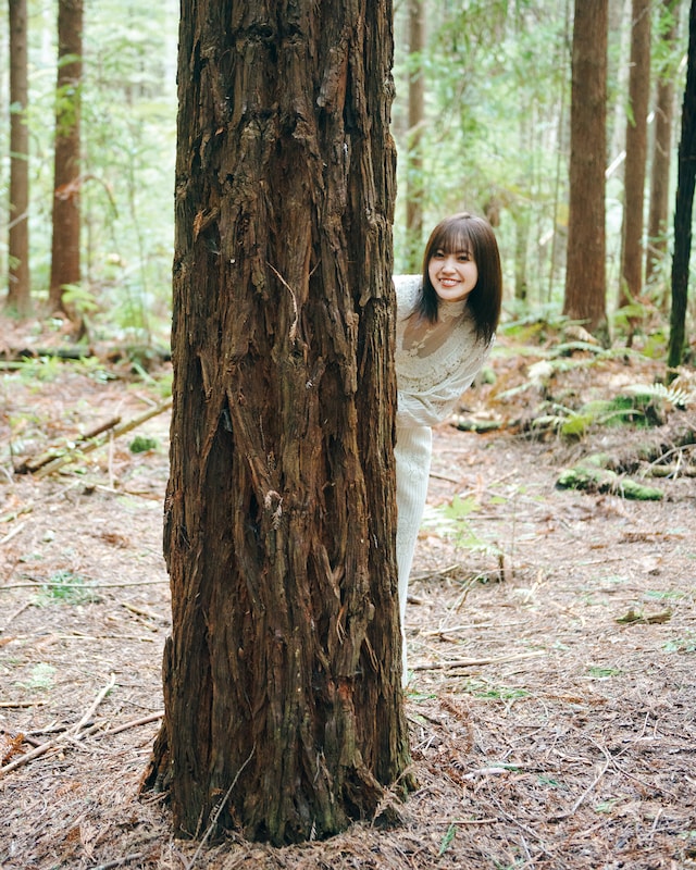 松田里奈（櫻坂46）1st写真集「まつりの時間」より、木陰から顔を出す松田里奈。（撮影：北浦敦子）