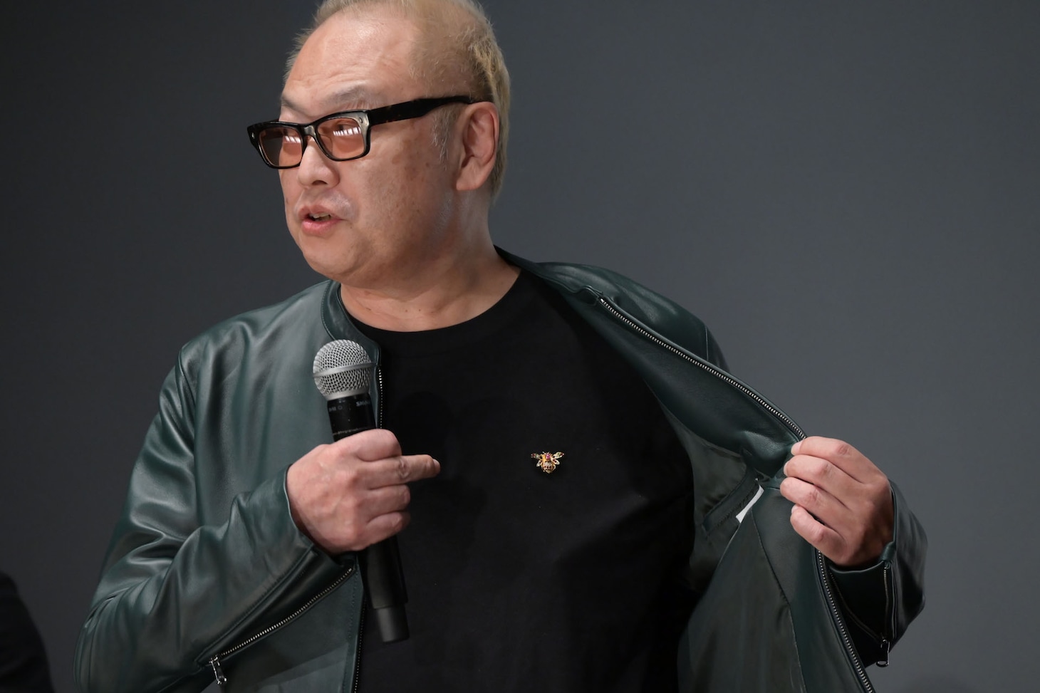 緑色のジャケットに蜂（8）のブローチという“タクヤ推し”ファッションの秋山純監督。
