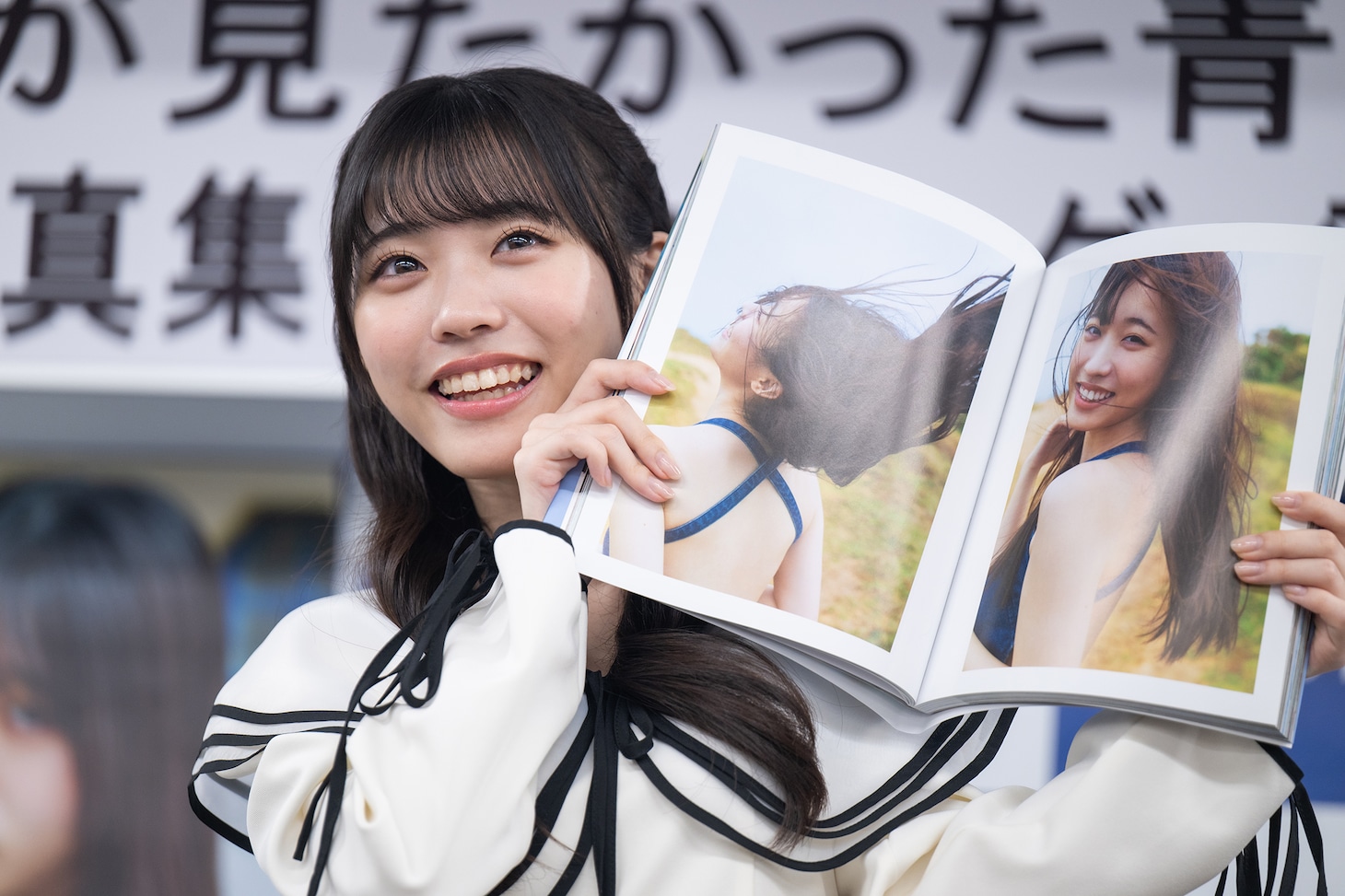 写真集からひょっこり顔を覗かせる金澤亜美。